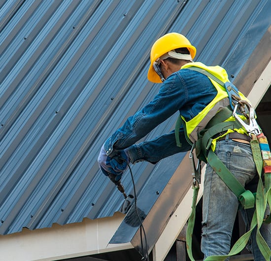Construction worker wearing safety harness belt during working on roof structure of building on construction site,Roofer using air or pneumatic nail gun and installing metal roof tile on top new roof.
