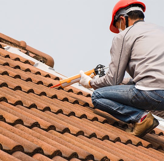 Technician man hand using glue gun with silicone adhesive or manual caulking gun with polyurethane to seal the leak on the roof. Installing and building construction concept.
